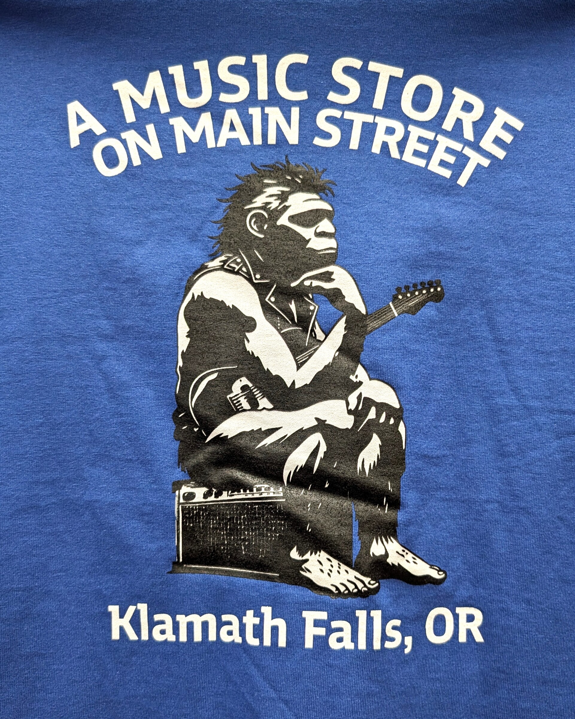 A Music Store on Main Street 100% Cotton T-Shirt, Neanderthal Rocker, Various Colors/Sizes