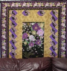 an Asia garden panel surrounded by gold dotted fabric with a ribbon chain of purpleand lavender with a striped inter boarder finished off with a huge floral outter border.