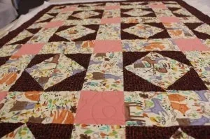 this quilt has big squares with a floral animal print  fabric with peach conerstones, with dark brown .