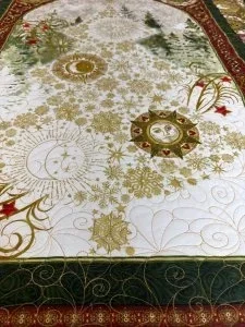 Quilted fabric featuring gold celestial designs, including sun, moon, and stars, with green and red decorative borders and intricate patterns.