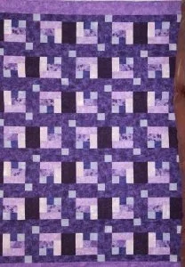 quilt featuringa pattern of purple, lavendar, and light bluesquares and rectangles with a solid black minkey backing