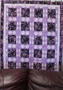 puple floral snowball quilt with deep purples, pinks, grassy spikes surrrounded by lavender sashing.